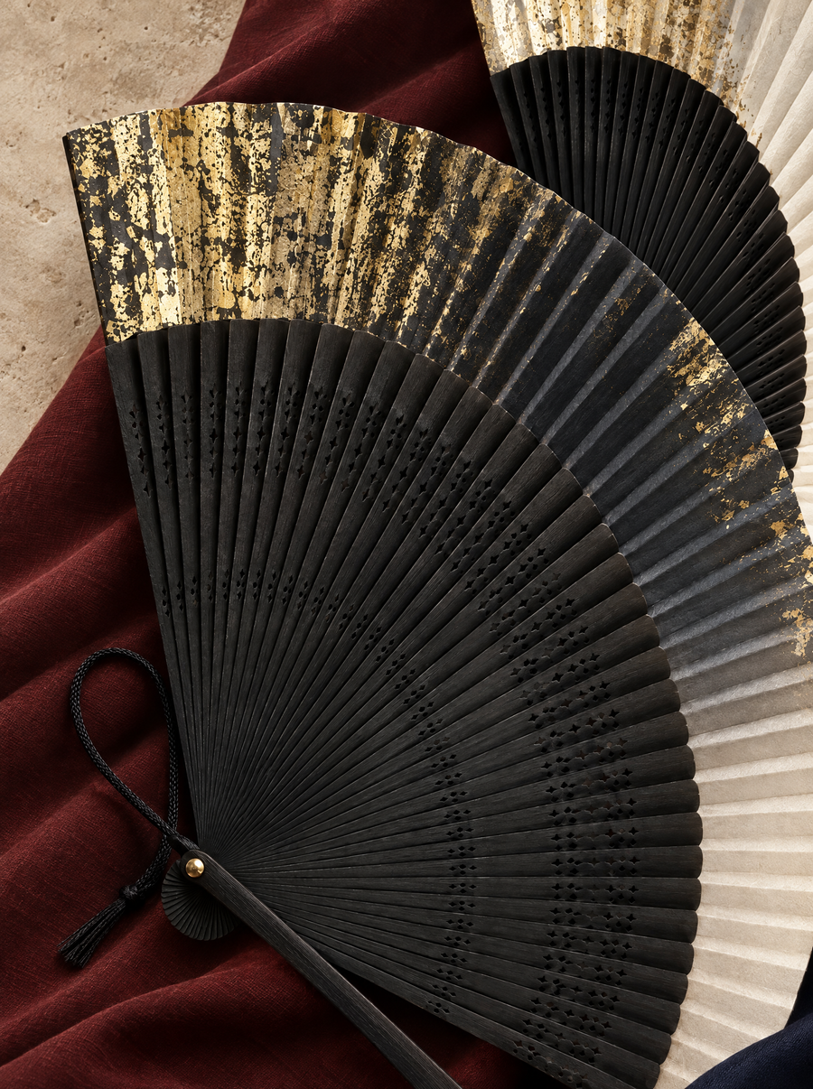 Black, gold and ivory folding fans on oxblood fabric and warm sand stone.