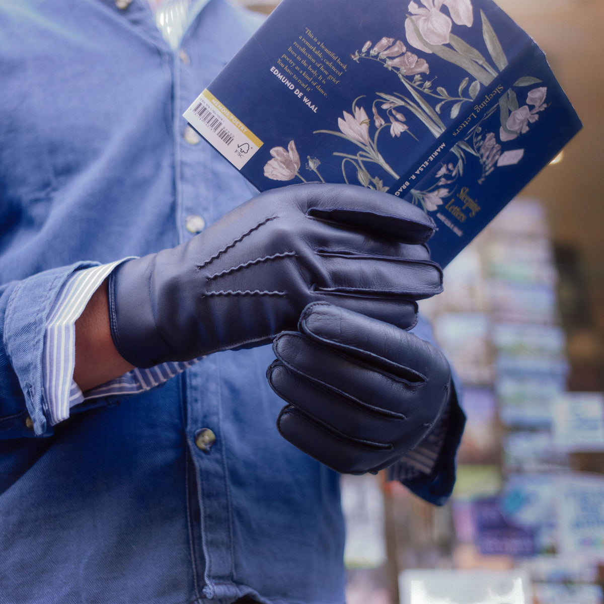 Close up of a man holding a book, wearing navy leather gloves.